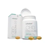 En beholder med CBD-kapsler med en æske mærket "Cibdol 5% CBD softgel kapsler 2.0 (60 stk – 8.3 mg)" og tre kapsler i forgrunden.